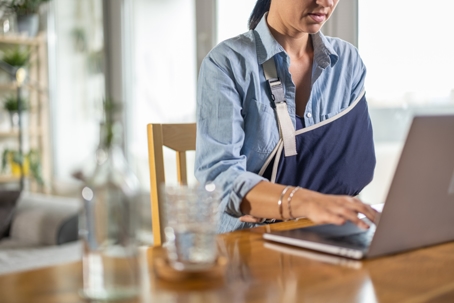 woman with injured arm sitting at the table and using laptop at home