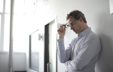 concerned man leaning against wall taking off glasses